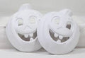 Two white unpainted ceramic pumpkin masks with cutout eyes and smiling toothy mouths.