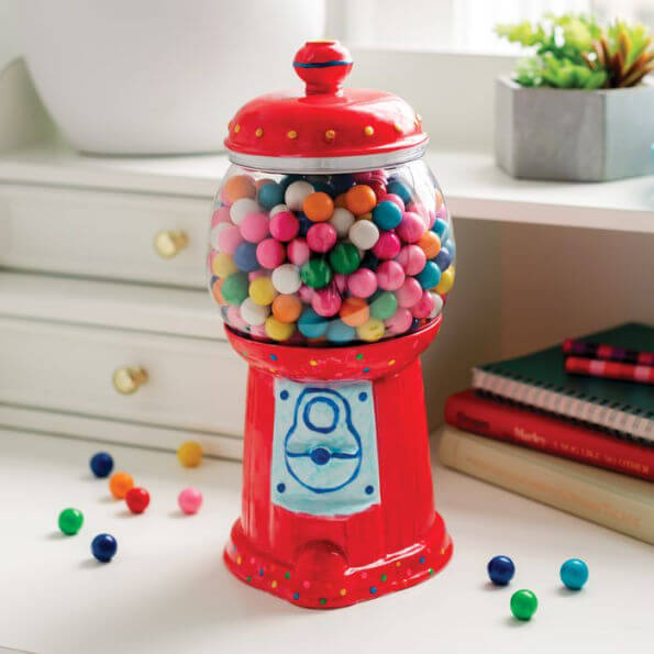 Hand-painted red ceramic gumball machine jar filled with colorful gumballs on a white desk.