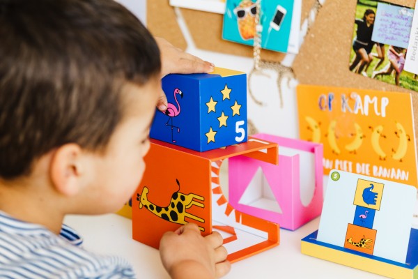 Child stacks a blue block with stars and a flamingo on an orange giraffe frame while playing Peek a Zoo.