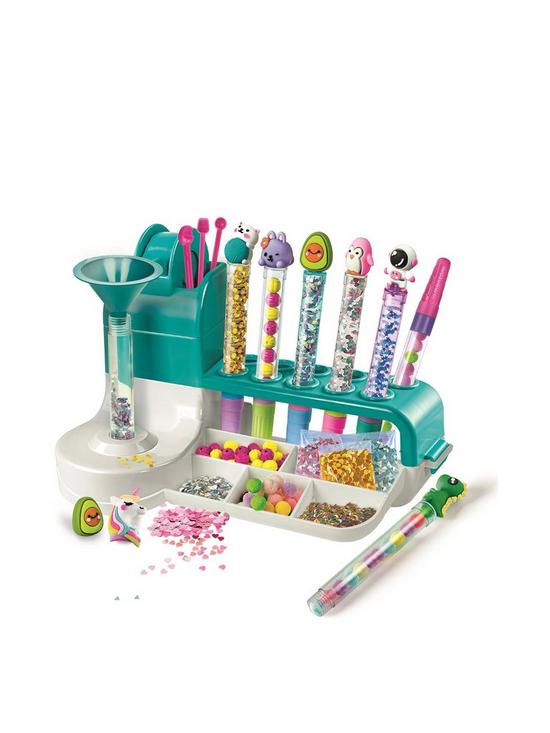 Teal pen-making station with funnel, glitter, and beads, featuring finished pens topped with cute animal characters.
