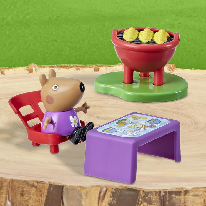 Peppa Pig figurine in a purple shirt sits at a purple table next to a red toy BBQ grill with yellow corn.