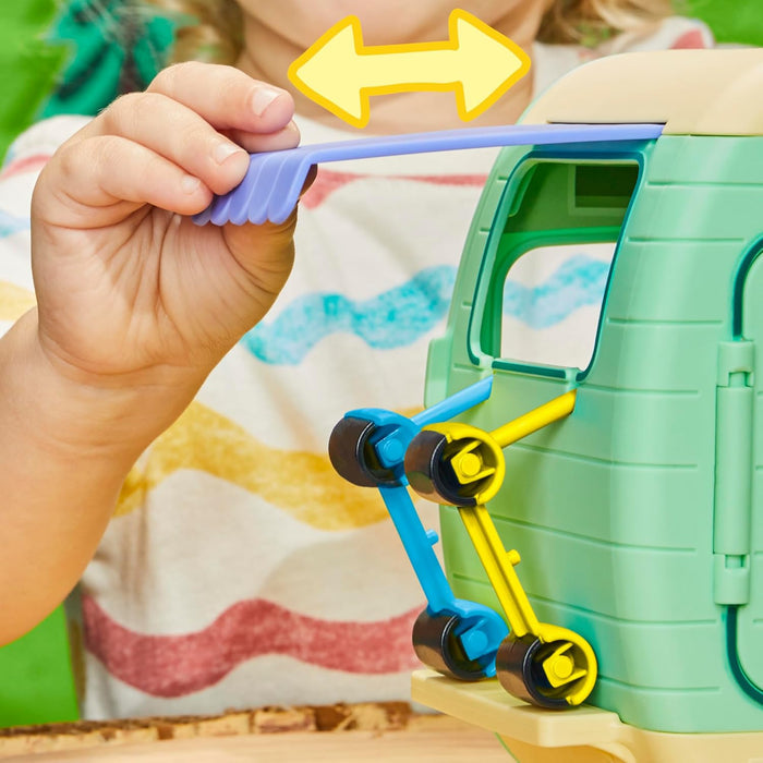 Child pulls a purple sliding awning out of a green toy caravan with blue and yellow scooters attached.