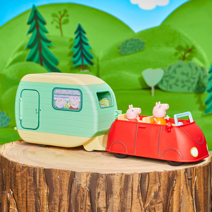 Peppa Pig figures in a red toy car towing a green and cream caravan on a tree stump against cartoon hills.