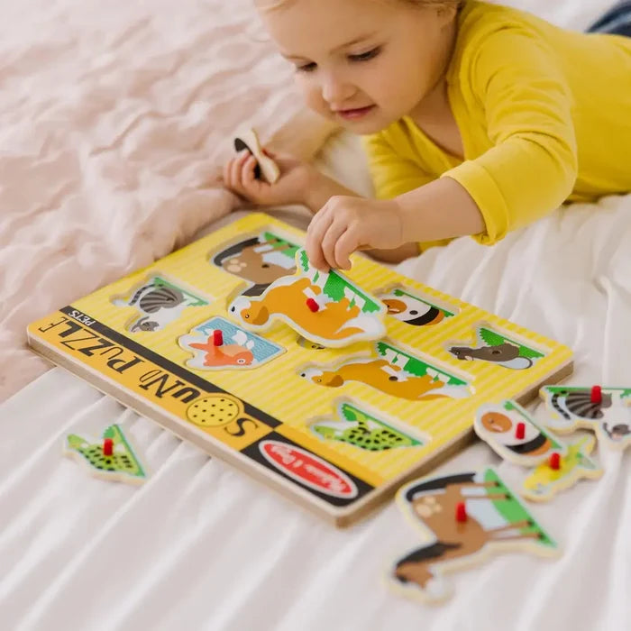 Toddler holds a wooden dog piece over a yellow striped peg puzzle featuring colorful pet illustrations.