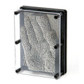 Rectangular black frame with clear front, housing silver metal pins that form a 3D impression of a human hand.