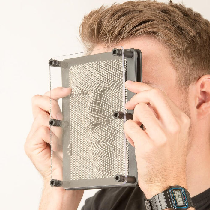 Silver metal pins in a black frame, creating a 3D facial impression behind a clear plastic cover.