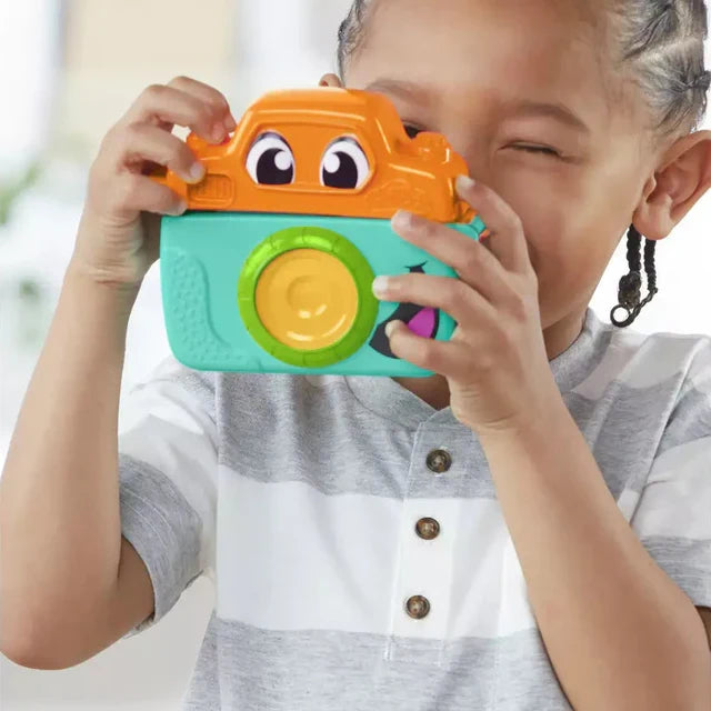Child holding an orange and teal toy camera with cartoon eyes and a circular yellow and green lens.