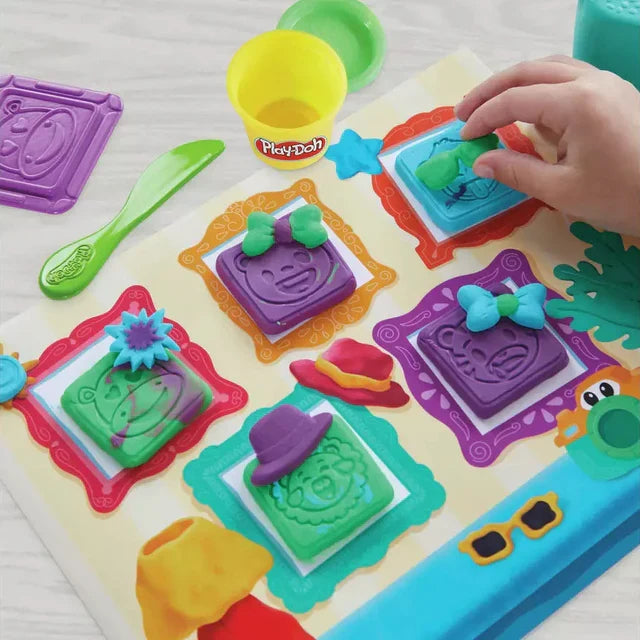 Child decorating Play-Doh animal faces with bows and hats on a camera-themed picture frame play mat.