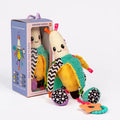 Plush banana baby toy with high-contrast patterns, teal textures, and orange star teether next to its box.
