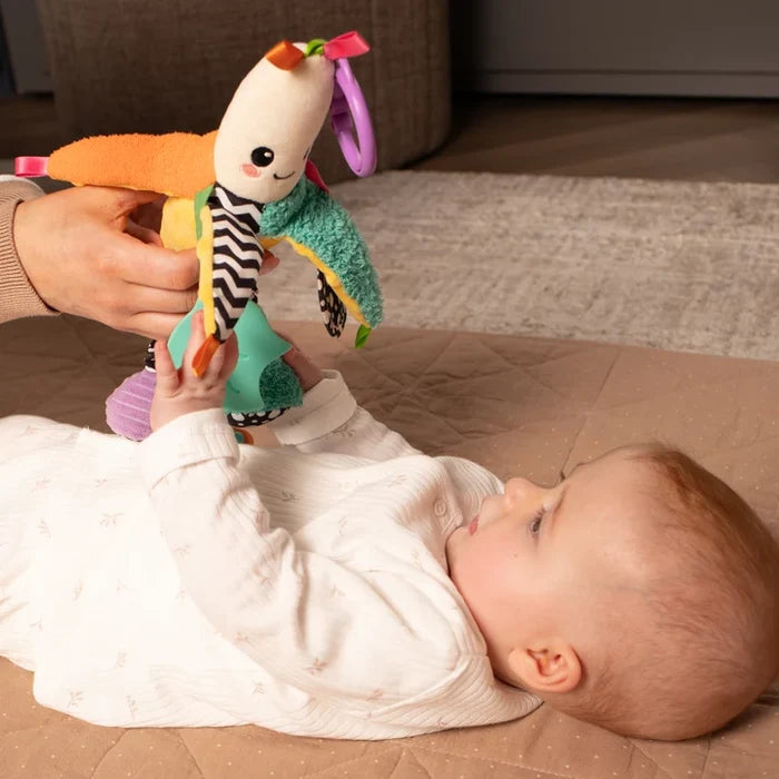 Colorful smiling plush banana toy with textures and chevron patterns held above a baby reaching up.