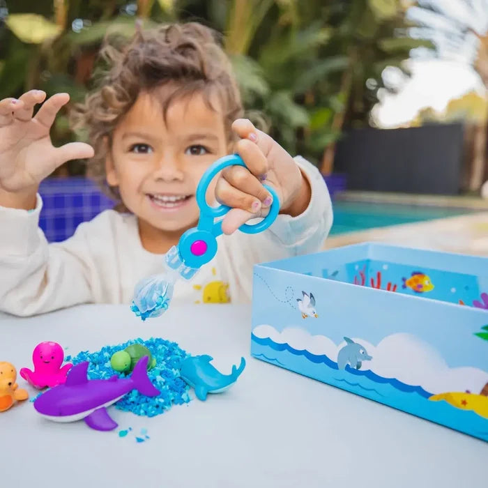 Child uses blue scooper with textured blue foam, colorful sea creature figures, and an ocean-themed box.
