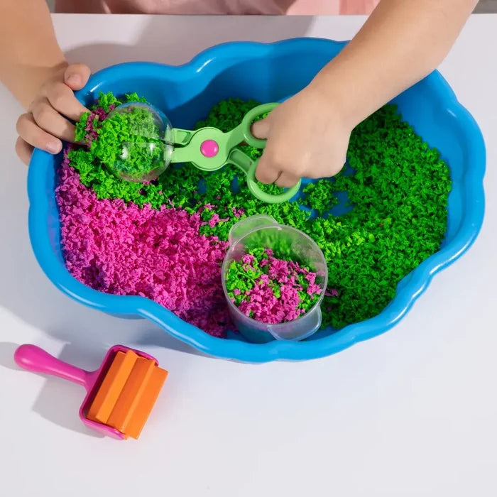 Child playing with green and pink foam in a blue cloud-shaped bin using a green scooper and roller tool.