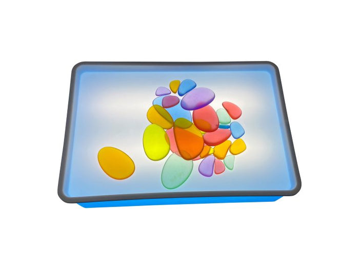 Rectangular blue light box with glowing surface and various colorful, translucent pebble-shaped blocks.