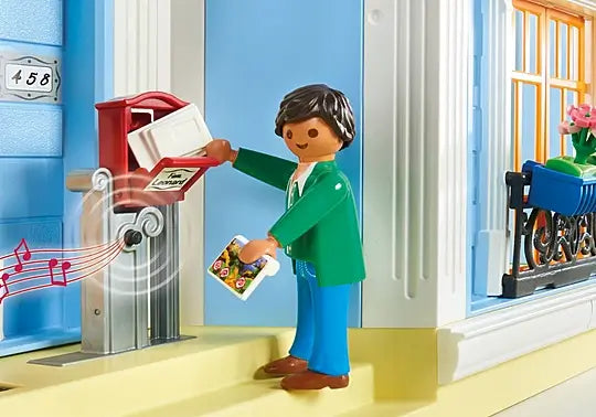 Playmobil man in green jacket puts mail into a red musical mailbox outside a blue dollhouse wall numbered 458.