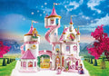 Detailed white and pink toy castle with towers, spiral stairs, and princess figures in a scenic mountain landscape.