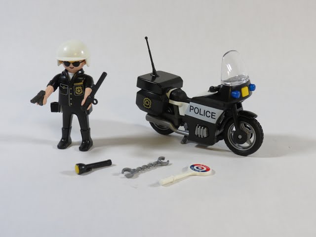 Playmobil police officer in black uniform, white helmet, black motorcycle with POLICE text, and small toy accessories.