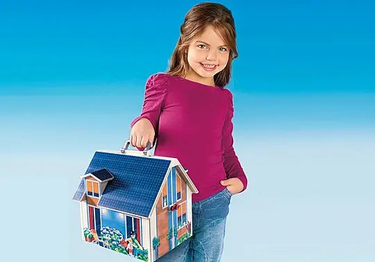 Young girl holding a portable toy house with a blue roof, white trim, and a silver carrying handle.
