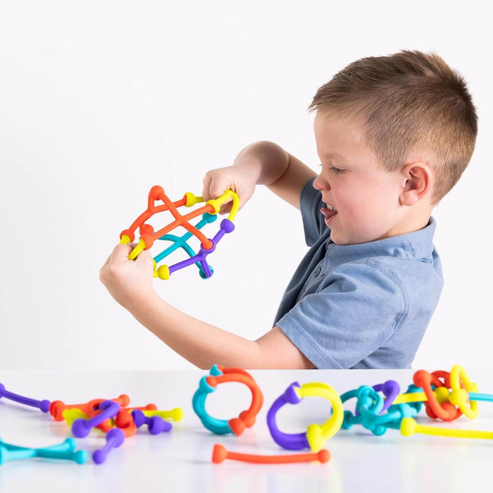 Young boy building with colorful, flexible silicone sticks and ring connectors on a white background.