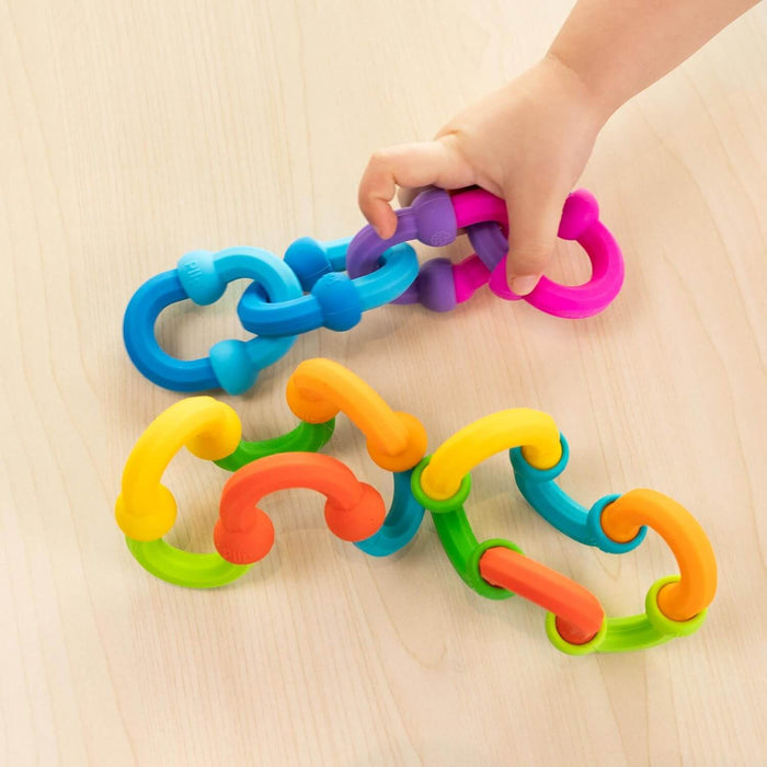 Child’s hand connecting colorful, flexible silicone links into chains on a light wood surface.