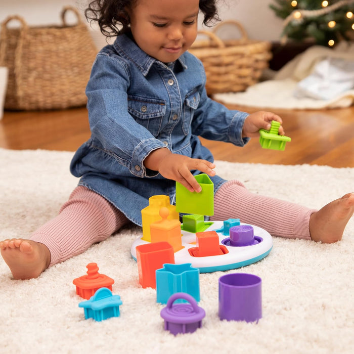 Toddler playing with colorful shape sorter toy on white rug with bright chunky blocks and a round white base.