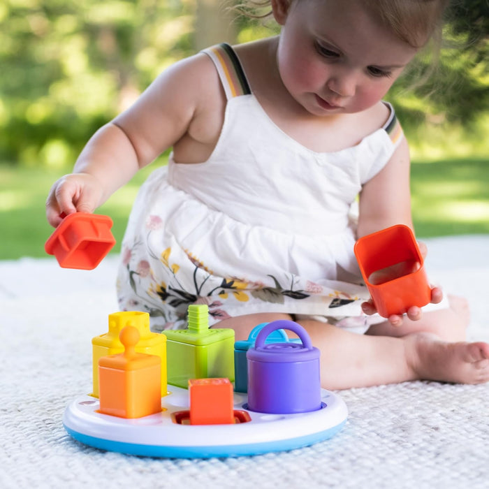 Toddler playing with bright orange, yellow, green, and purple geometric blocks on a circular base.