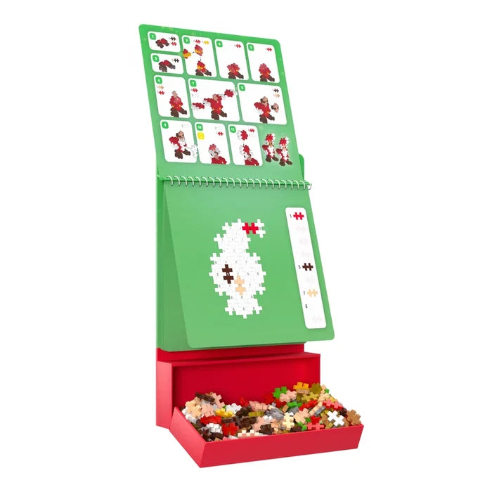 Green Christmas flip-chart activity pad with a red tray of colorful plus-shaped pieces and a snowman on the easel.