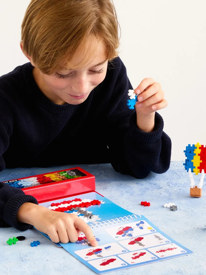 Boy builds transportation toys using a spiral activity pad and colorful, cross-shaped interlocking pieces.