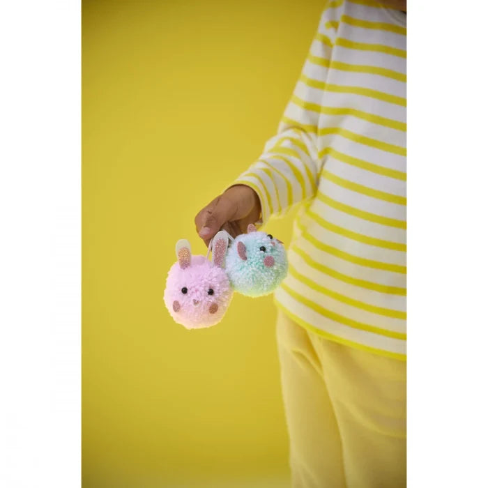 Child holding a pink and a light blue pom-pom bunny craft with glittery ears and bead eyes.