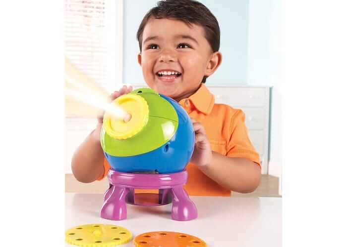 Smiling child with a blue and green spherical projector on a purple stand, shining light from its yellow lens.