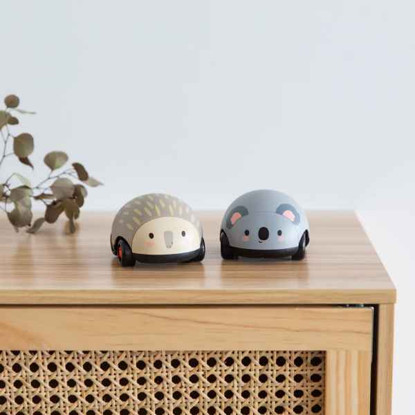 Two round pull-back toy cars shaped like a tan echidna and a grey koala sitting on a light wood surface.