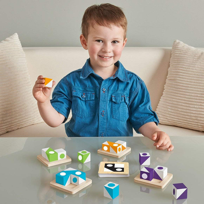 A boy plays with green, orange, blue, and purple patterned wooden cubes, matching them to challenge cards.