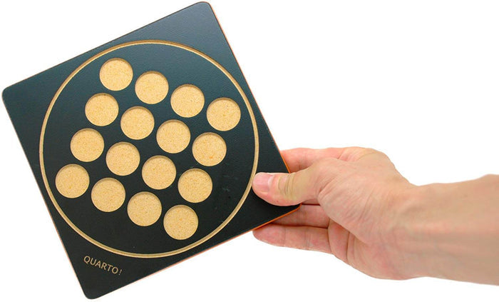 Hand holding a black square board game with a 4x4 grid of circular slots, gold border, and Quarto! text.