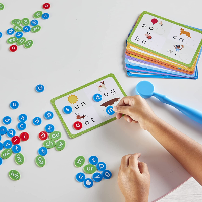 Child placing colorful magnetic letter tiles onto word cards with pictures, next to a blue magnetic wand.