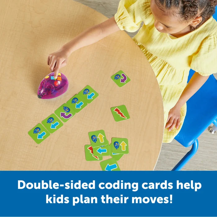 A child presses buttons on a purple translucent mouse robot next to green coding cards with directional arrows.