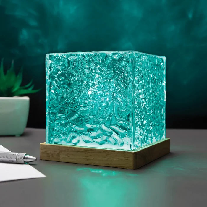 Teal cube lamp with a rippled water-effect texture glowing on a square wooden base.