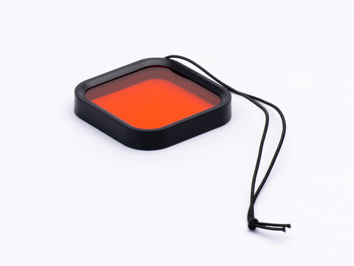Square filter with orange color on a black frame, attached to a string on a white background