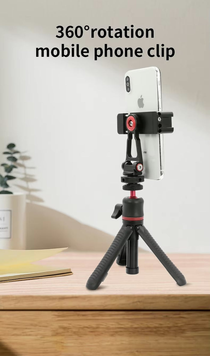 A mobile phone held in a 360-degree rotating clip attached to a small tripod on a wooden desk, showing the phone mounted vertically