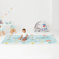 Baby sitting on a rectangular light blue playmat featuring a world map pattern with animals and travel icons.