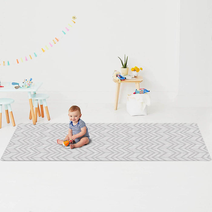 Large grey and white chevron-patterned playmat on a white floor with a baby sitting on it in a bright playroom.