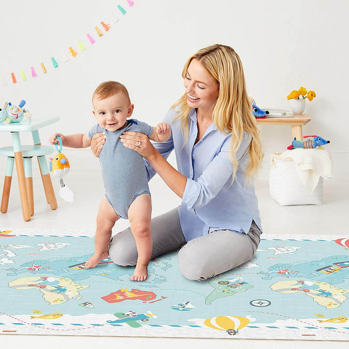 Woman holding a baby on a light blue foam playmat featuring a colorful world map and animal illustrations.