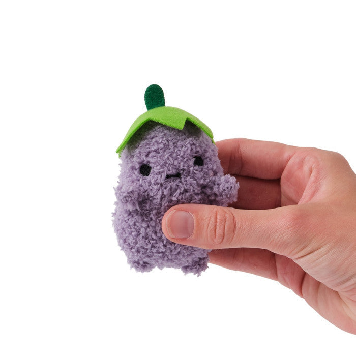 Tiny purple fuzzy plush with a green leaf hat and small black eyes, held by a hand to show scale.