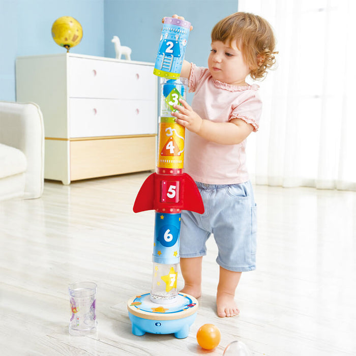 Toddler stacking colorful numbered tubes to build a rocket-shaped air stacker toy.