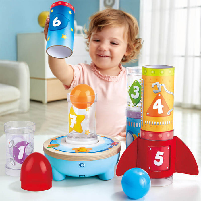 Toddler stacking numbered colorful tubes over a floating orange ball on a blue rocket-themed air-powered toy.