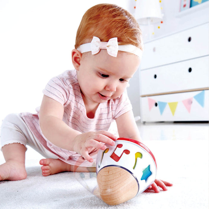 Baby girl playing with a wooden-based music box featuring colorful music notes and a clear rotating dome.