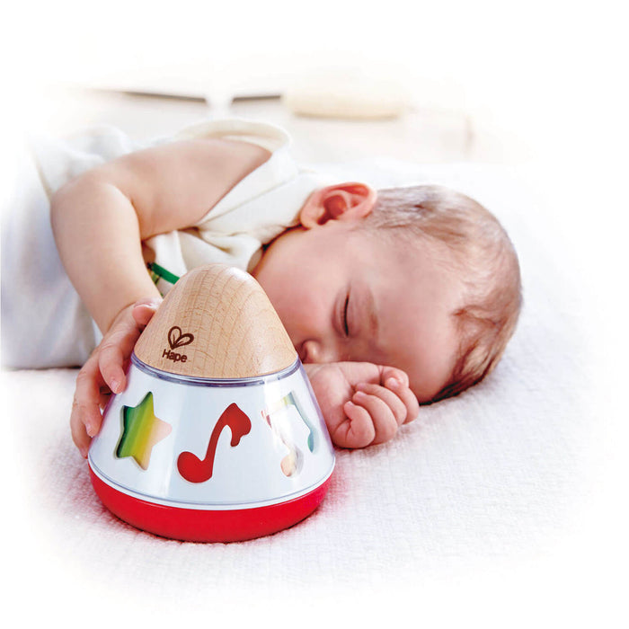 Sleeping baby next to a cone-shaped wooden Hape music box with colorful notes and a red base.
