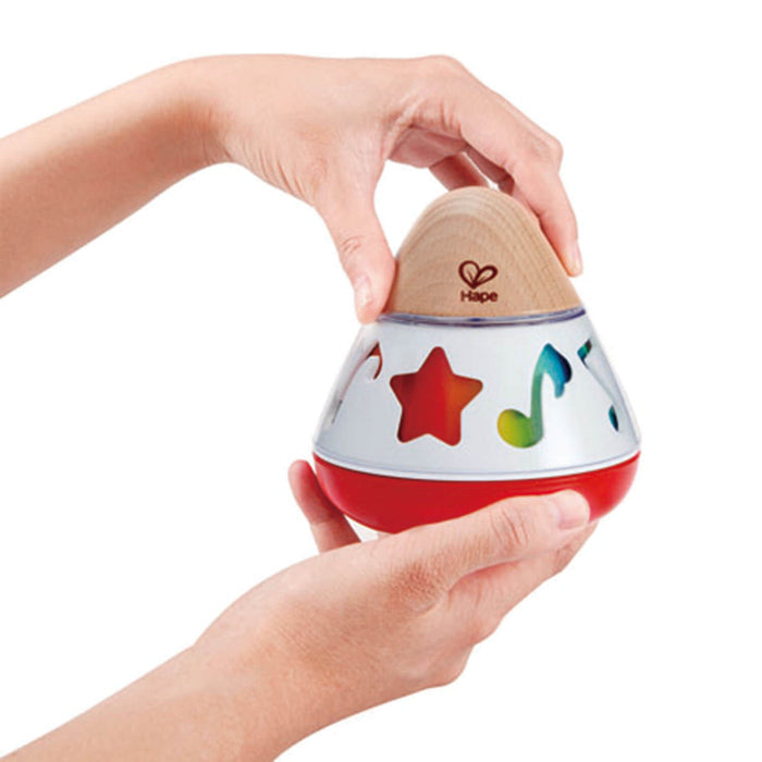 Hands rotate a cone-shaped wooden music box with colorful notes and a red star on a white and red base.