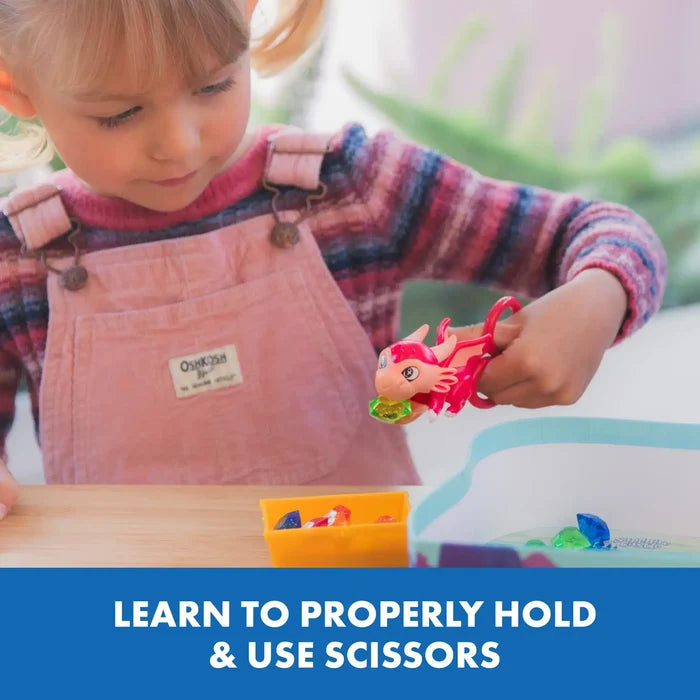 Young girl uses red dragon-shaped scissors to pick up a green toy gem from a colorful sorting game.