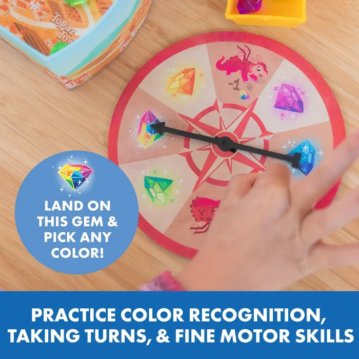 A hand spins the black pointer on a round game spinner featuring colorful gem icons and a red dragon.