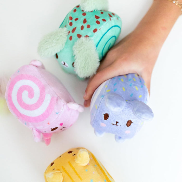 Hand holds a purple bunny squish plush among pink, green, and yellow animal-shaped plush toys.
