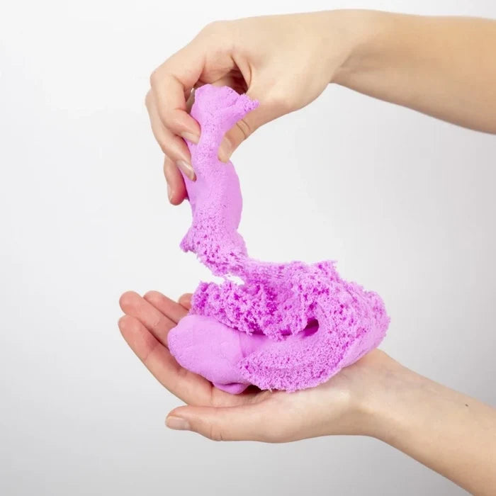 Hands pulling apart vibrant pink, fluffy, textured sensory compound against a white background.